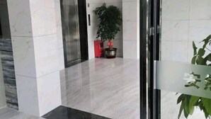 Un hall d’entrée avec un sol en marbre, une porte en verre et une plante en pot.