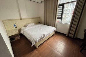 Een hotelkamer met een bed, nachtkastje, raam met gordijnen en uitzicht op gebouwen.