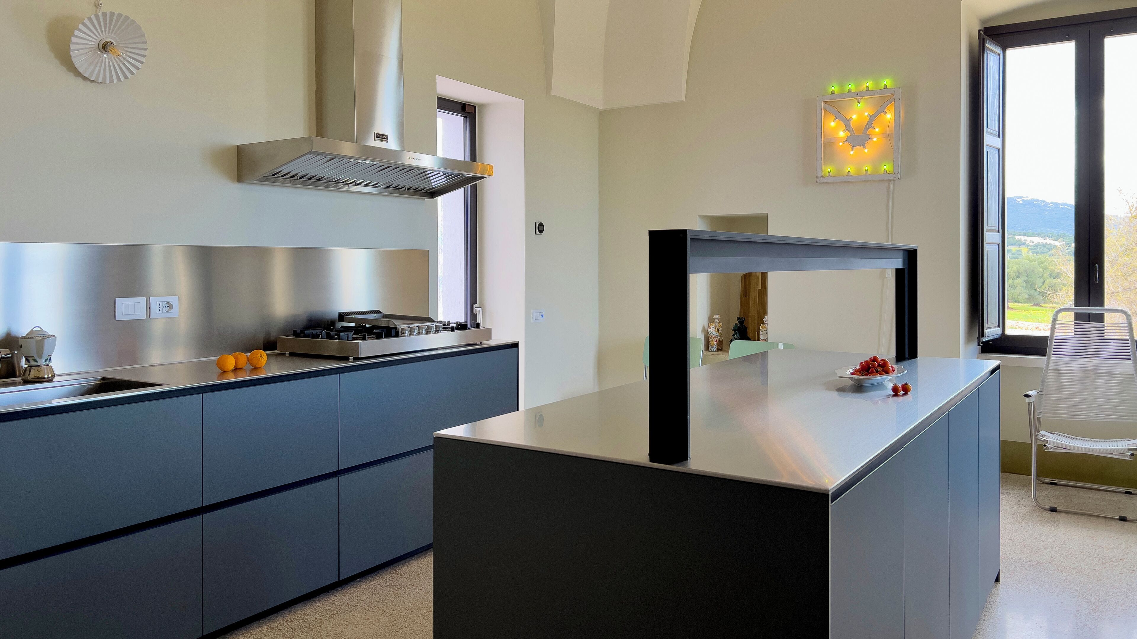 Une cuisine moderne dotée d’une cuisinière intégrée, d’une hotte aspirante et d’une grande fenêtre offrant une vue sur l’extérieur.