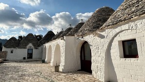 Egy udvar, melyben fehér kőből épült épületek állnak, ezeknek kúp alakú tetőik és íves bejáratuk van.