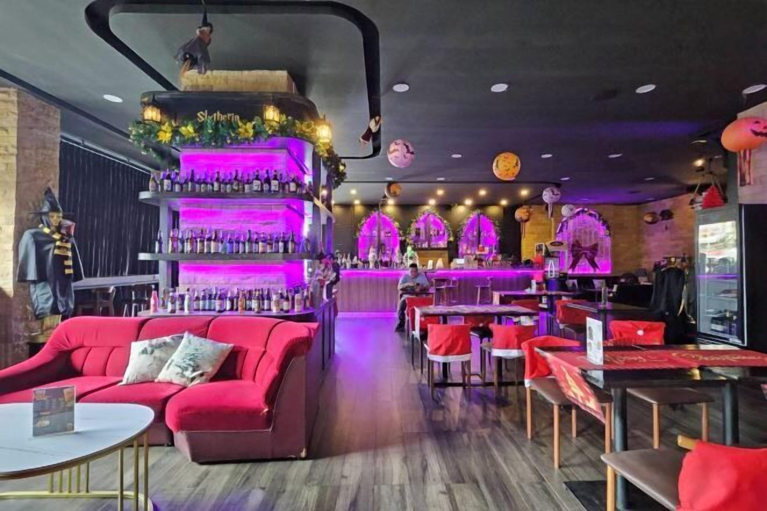 A bar area with a multi-tiered shelf of bottles, red seating, and a counter.