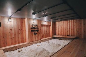 A wooden spa room with a massage bed, a wall-mounted sign, and a wooden floor. - Oscar Palace Hotel & Wellness Center (Sadao)