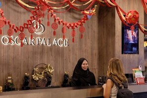 Un mostrador de recepción en OSCAR PALACE con un fondo de madera, una araña y una pantalla digital que muestra contenido.