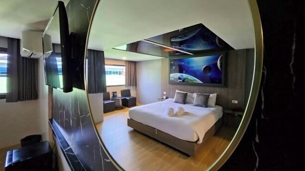Een slaapkamer met een bed, een televisie, een ruimteafbeelding en een bolle spiegel.