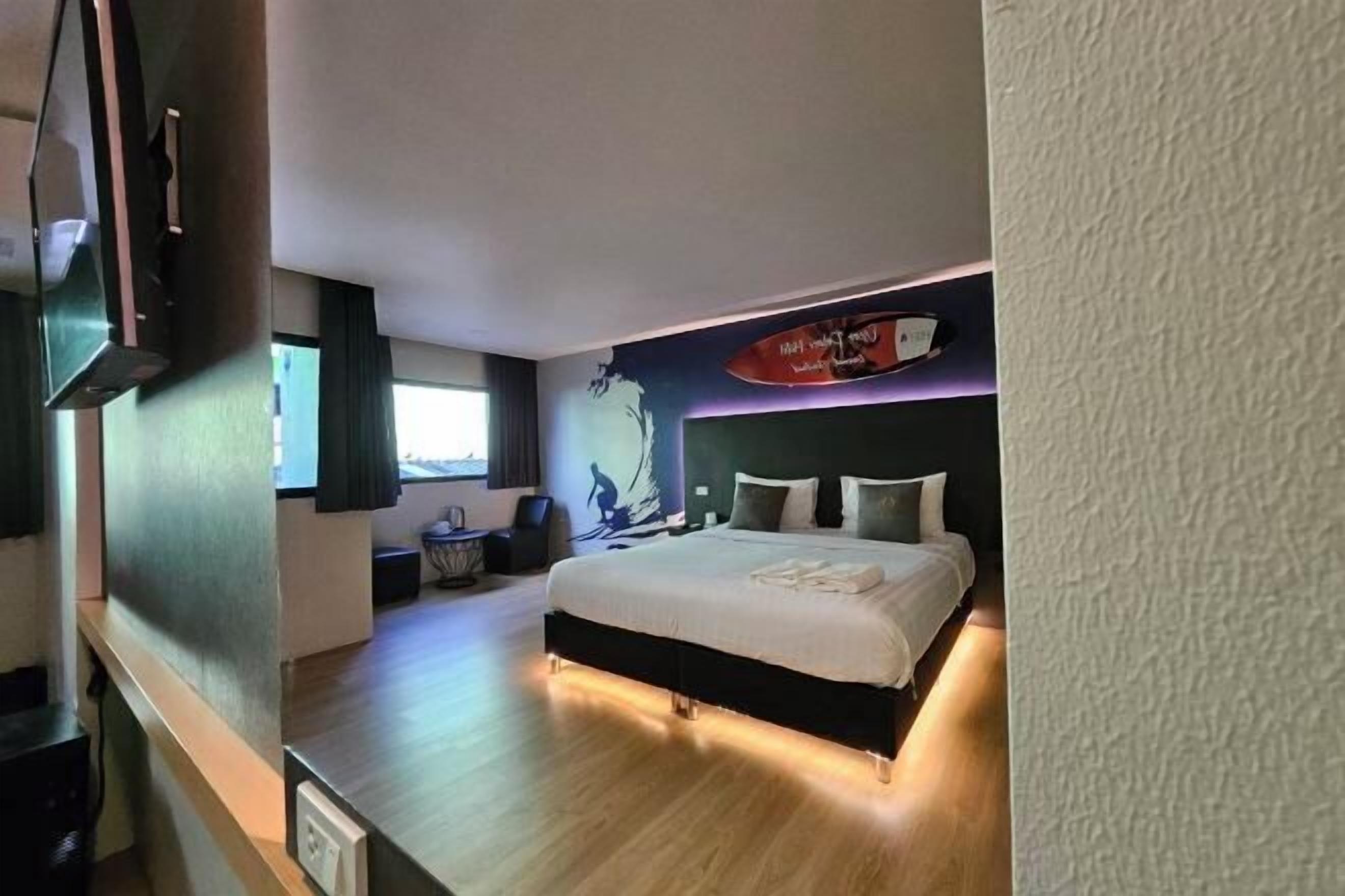 A modern hotel room with a large bed, a flat-screen TV mounted on the wall, and a ceiling-mounted light fixture.