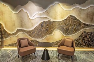 Una habitación con dos sillones y una mesa redonda, una pared texturizada con un diseño ondulado, y suelo cubierto de alfombra.