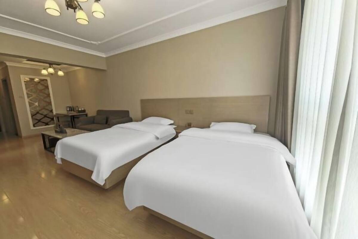 A hotel room with two beds, a sitting area, a mirror, and a ceiling light fixture.