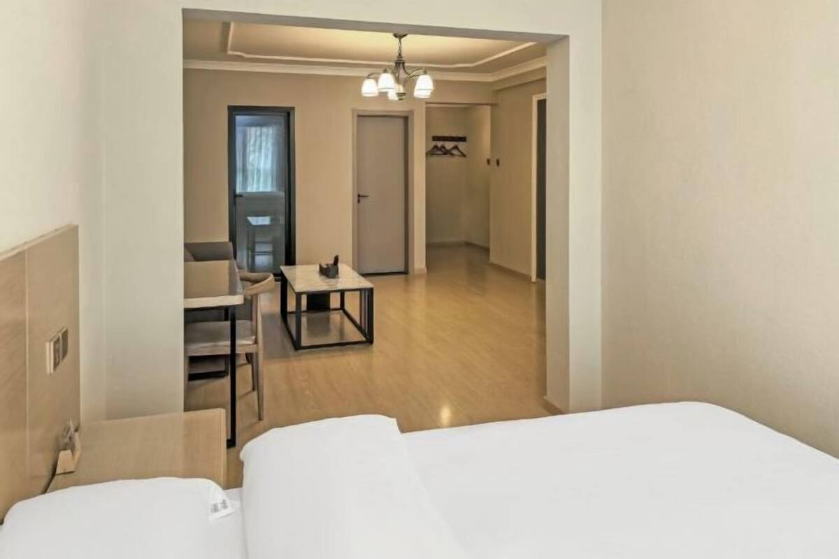 A hotel room with a bed, a desk, and a chair. There is a door leading to another room.
