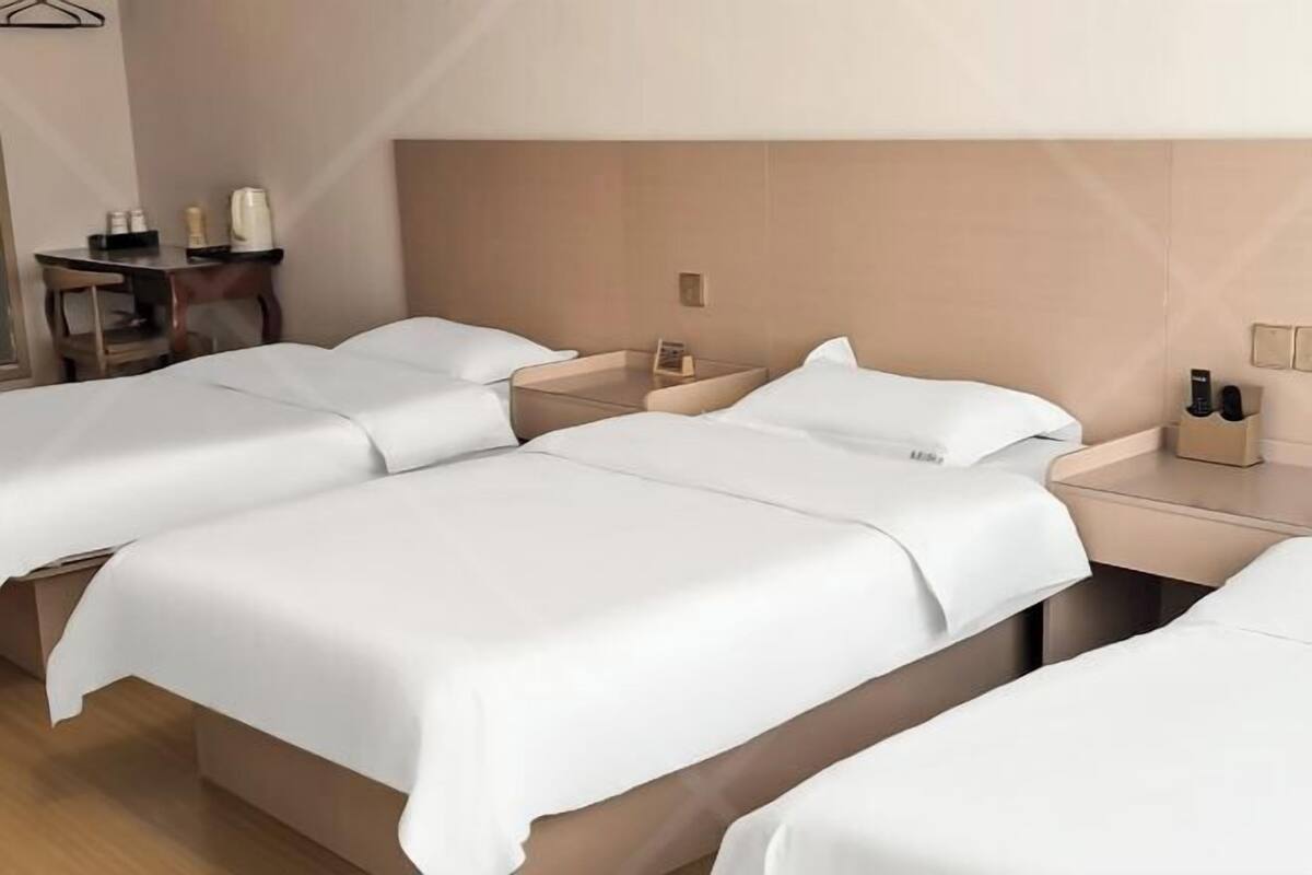 A hotel room with three beds, a small table with a chair, and a nightstand with a phone and a lamp.