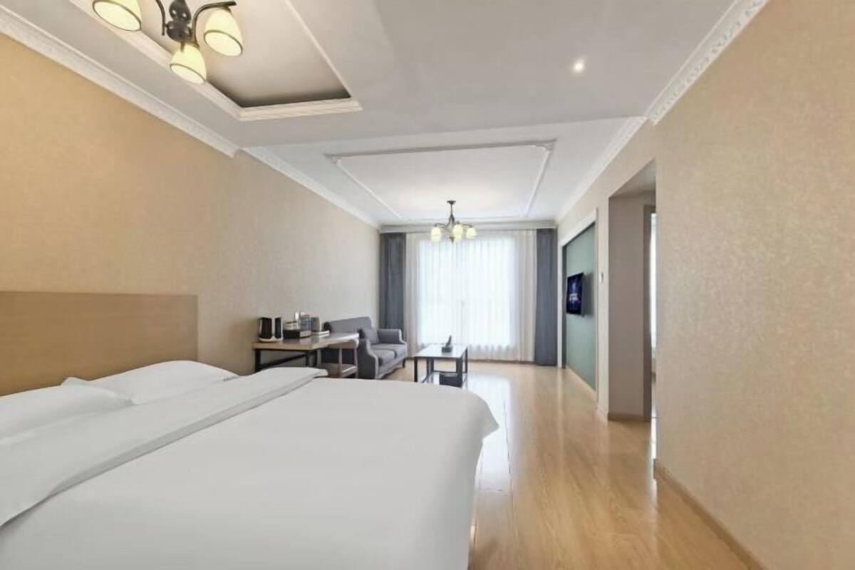 A hotel room with a large bed, a desk with a chair, a television, and a chandelier.
