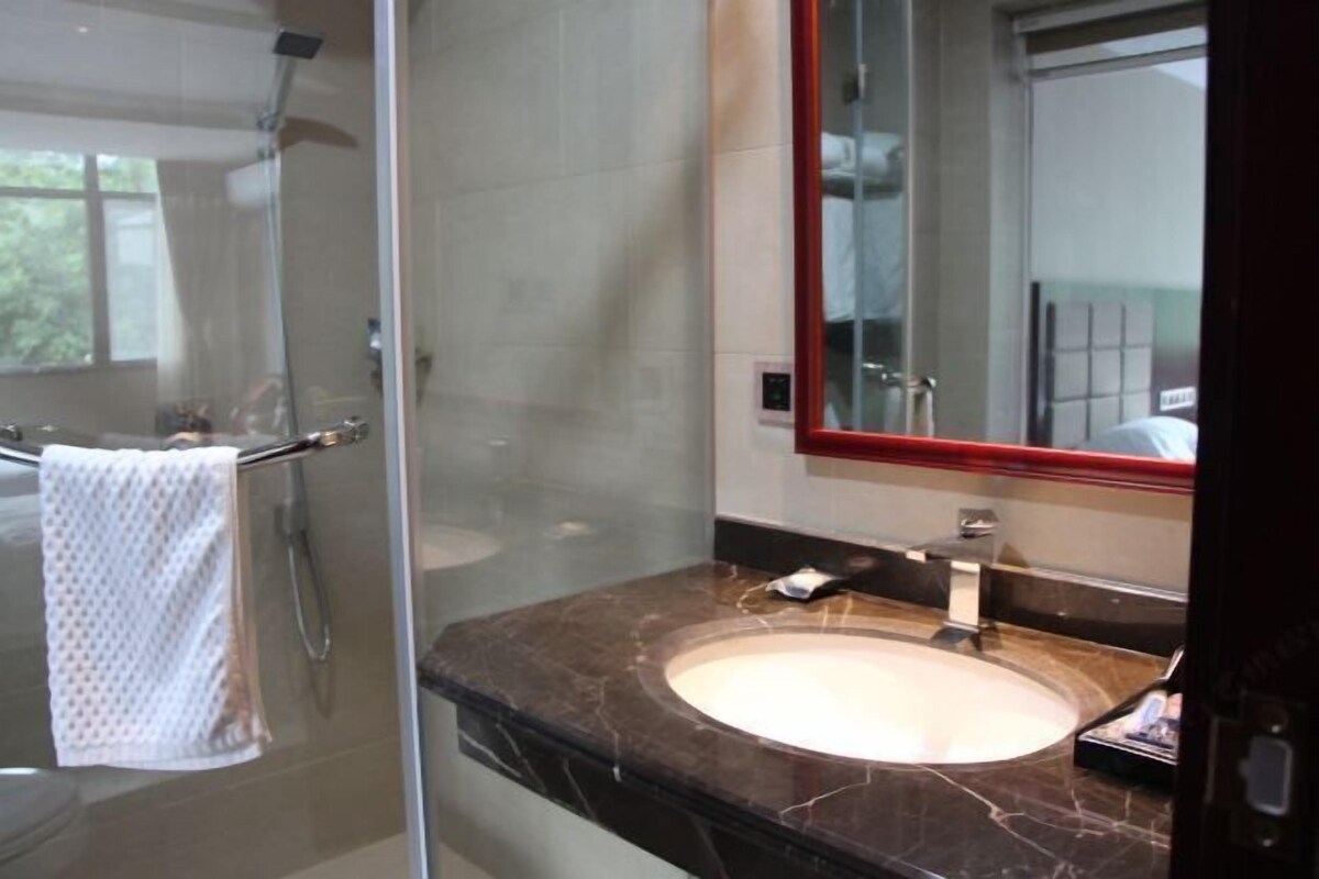 Une salle de bain dotée d’une douche à parois de verre, d’un comptoir en marbre, d’un lavabo et d’un miroir avec un cadre rouge.