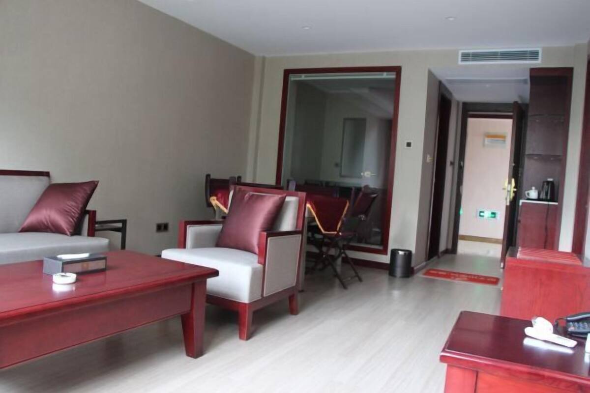A modern hotel room with a grey sofa, a red coffee table, and a dining area with a chair and table.