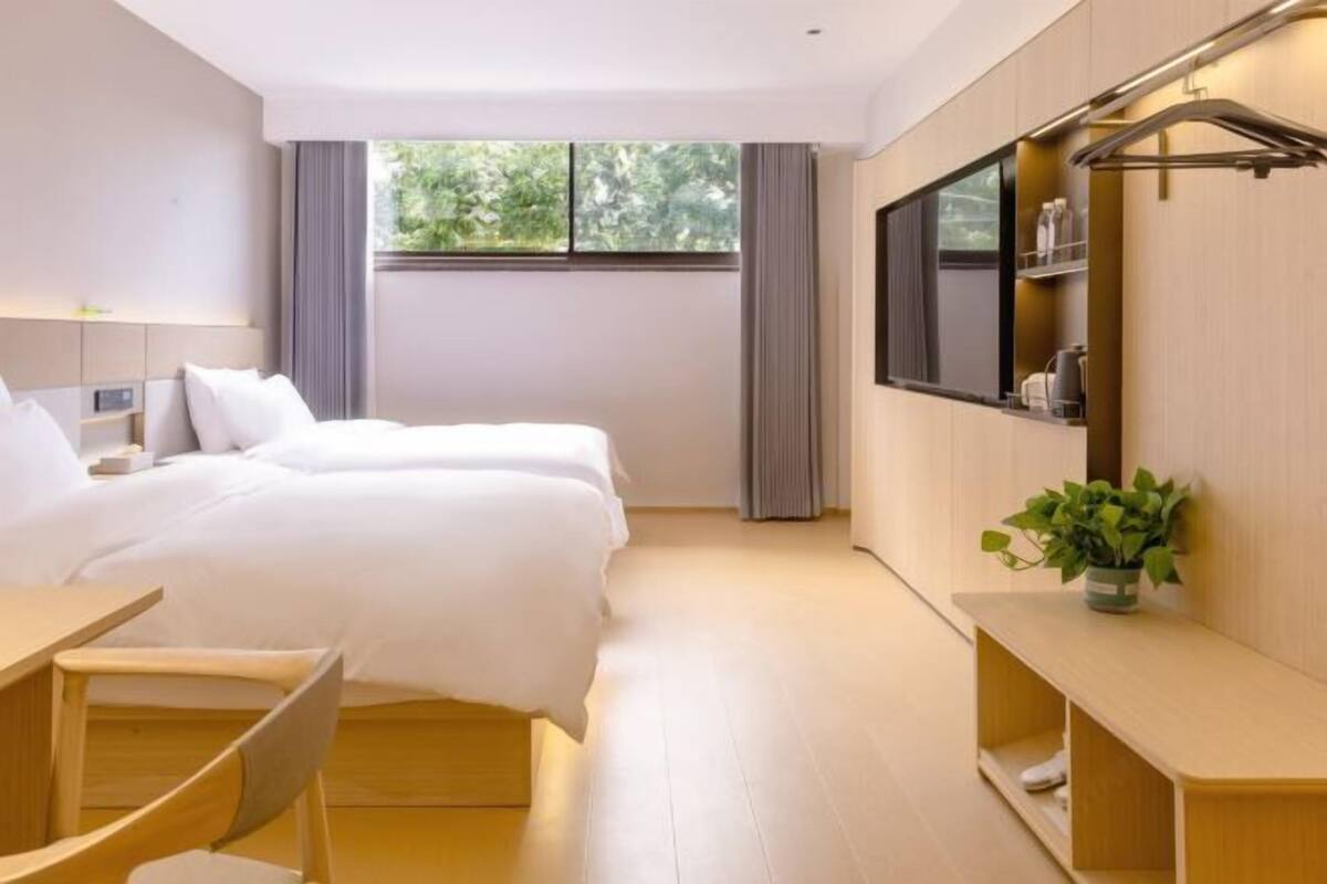 A modern hotel room with a bed, bedside table, TV, and a window with curtains.