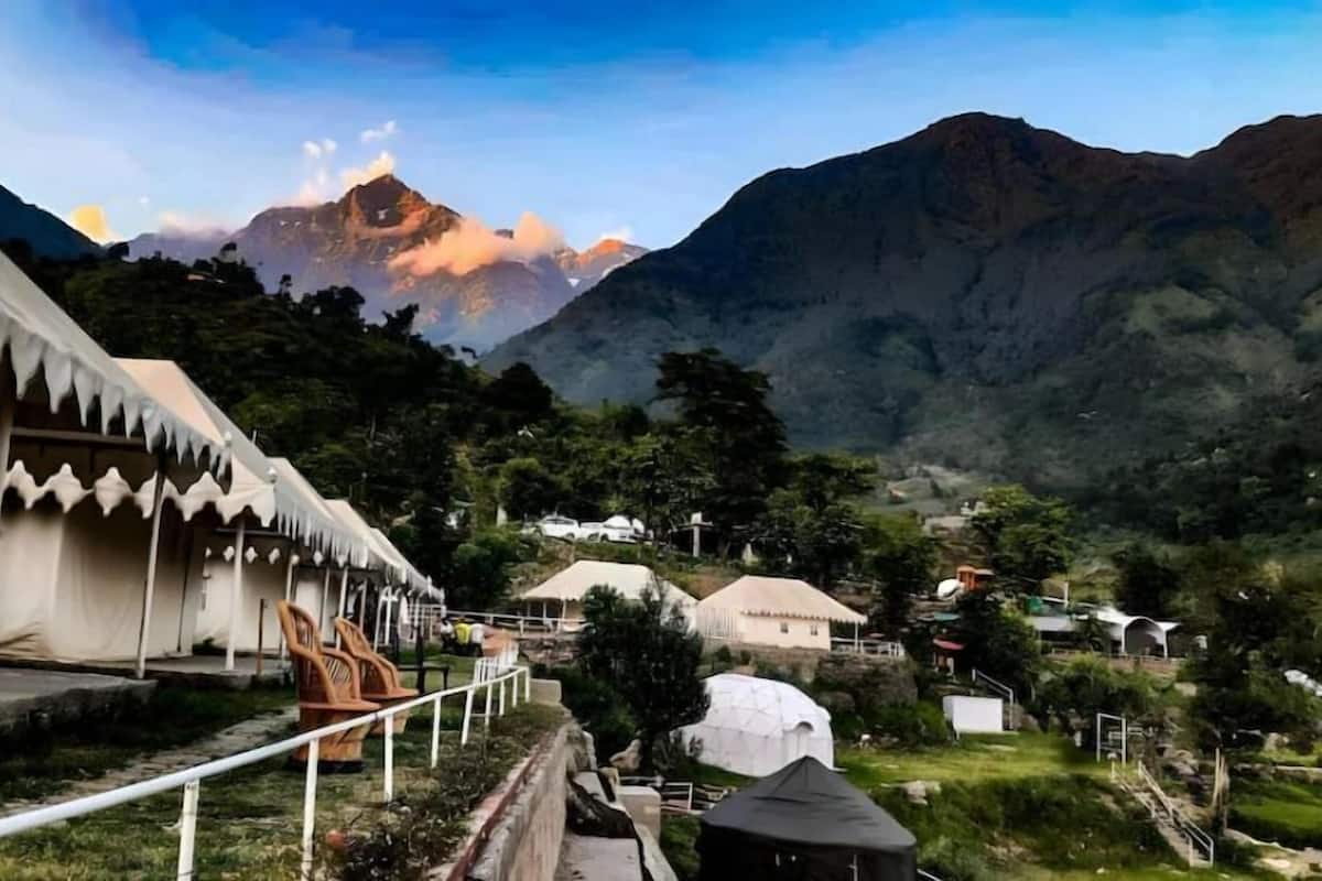 A mountainous landscape with a white building featuring a zigzag roof design, surrounded by greenery and other structures.
