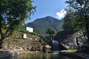 Un mur de pierres avec une pancarte, une cascade et une montagne en arrière-plan.