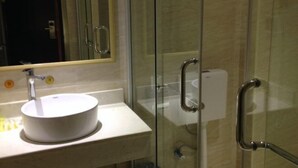 A bathroom with a round white sink, a mirror, and a glass shower enclosure.