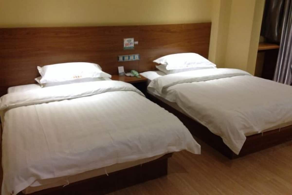 Hotellihuone, jossa on kaksi erillistä sänkyä, puinen pääty, yöpöytä, jossa on puhelin, ja pieni hylly, jossa on joitain tavaroita.