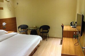 A hotel room with a bed, two chairs, a small table, a television, and a wooden desk with a kettle and bottles. - Tanghe Inn, Yucheng (Rucheng)