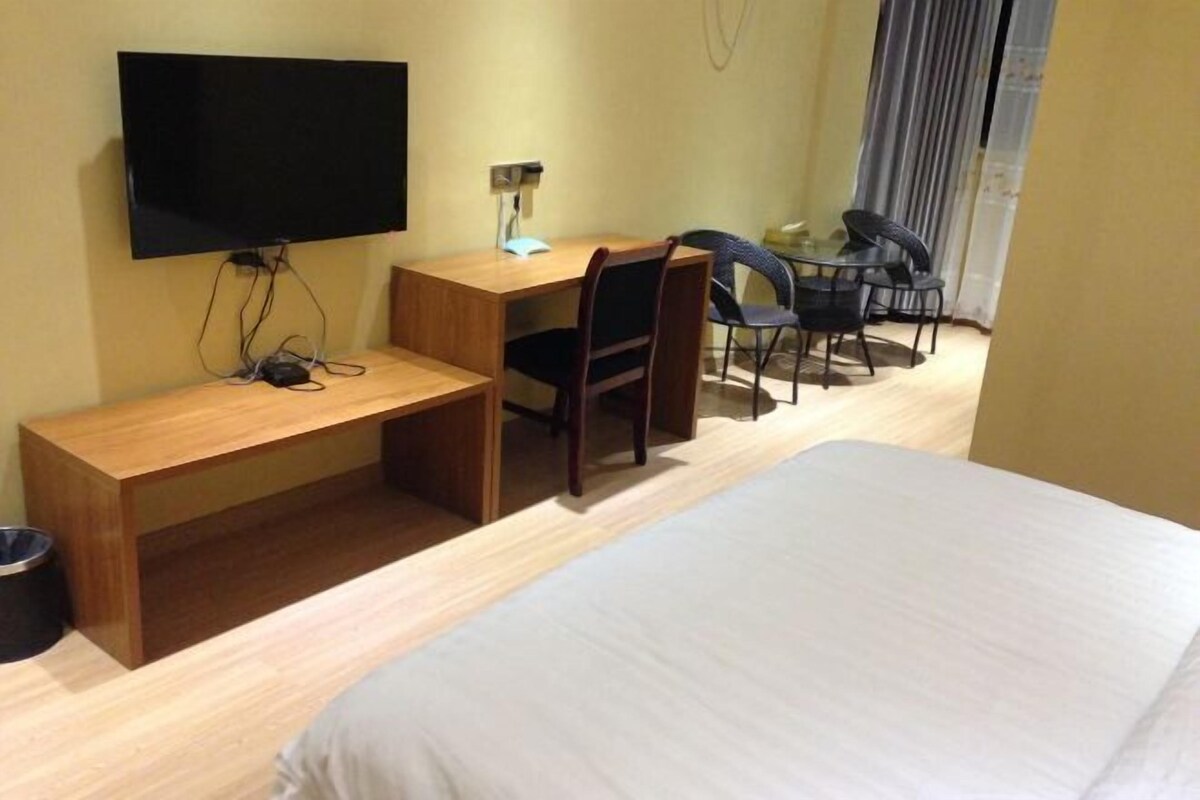 A hotel room with a bed, a desk with a chair, a television, and a small table.