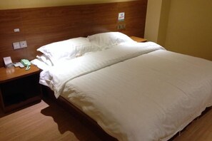 A hotel room with a wooden headboard, a bed with white linens, a bedside table with a phone and a lamp, and a wall-mounted power outlet. - Tanghe Inn, Yucheng (Rucheng)