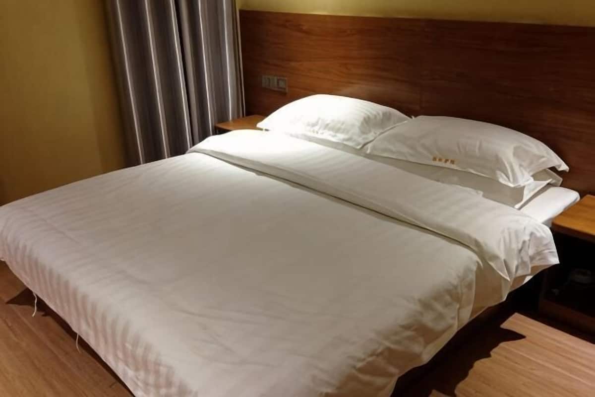 Siististi pedattu sänky, jossa on valkoiset lakanat, puinen pääty ja yöpöytä, jossa on lamppu.