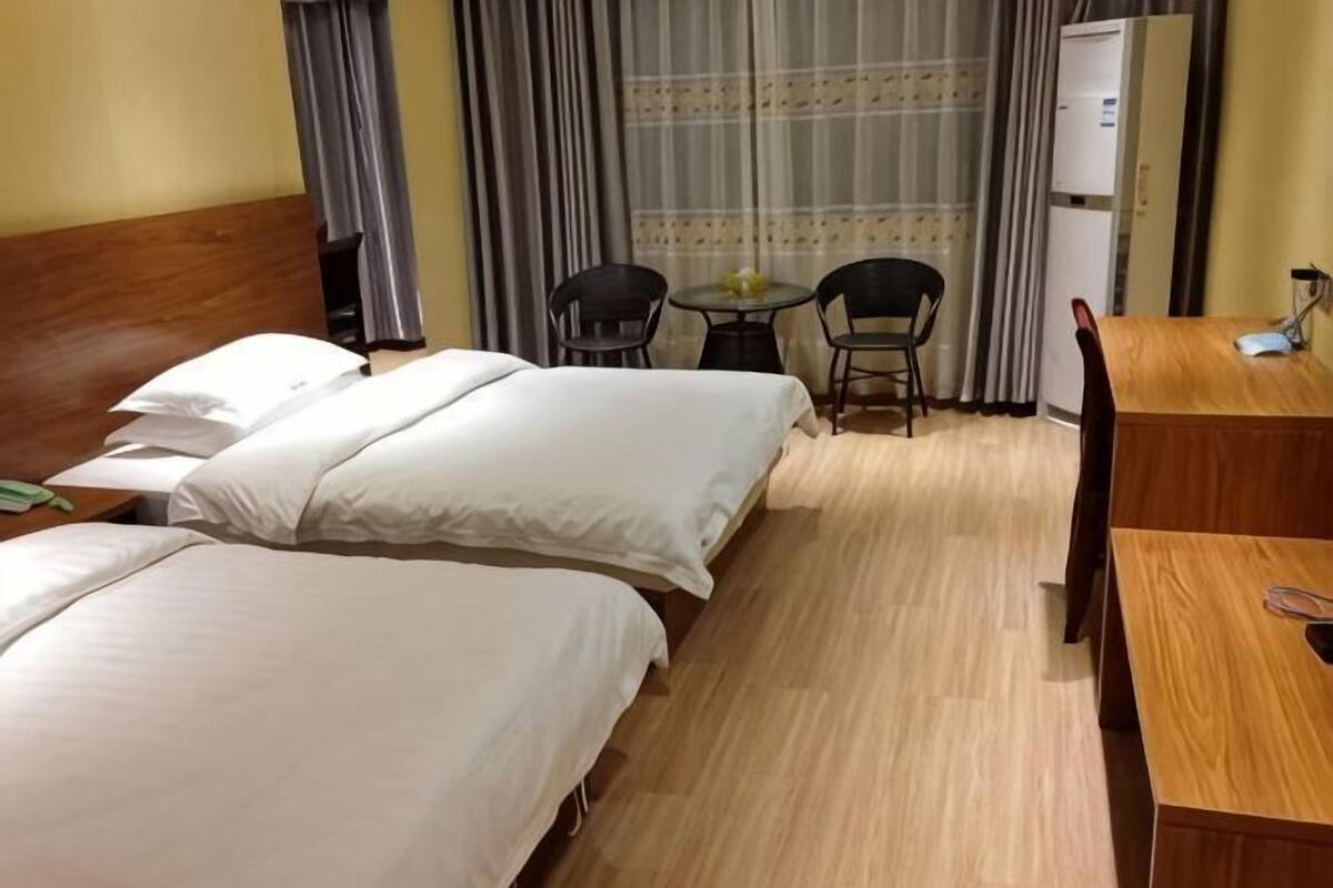 Hotellihuone, jossa on kaksi sänkyä, puinen pääty, työpöytä, tuoli ja pieni pöytä.