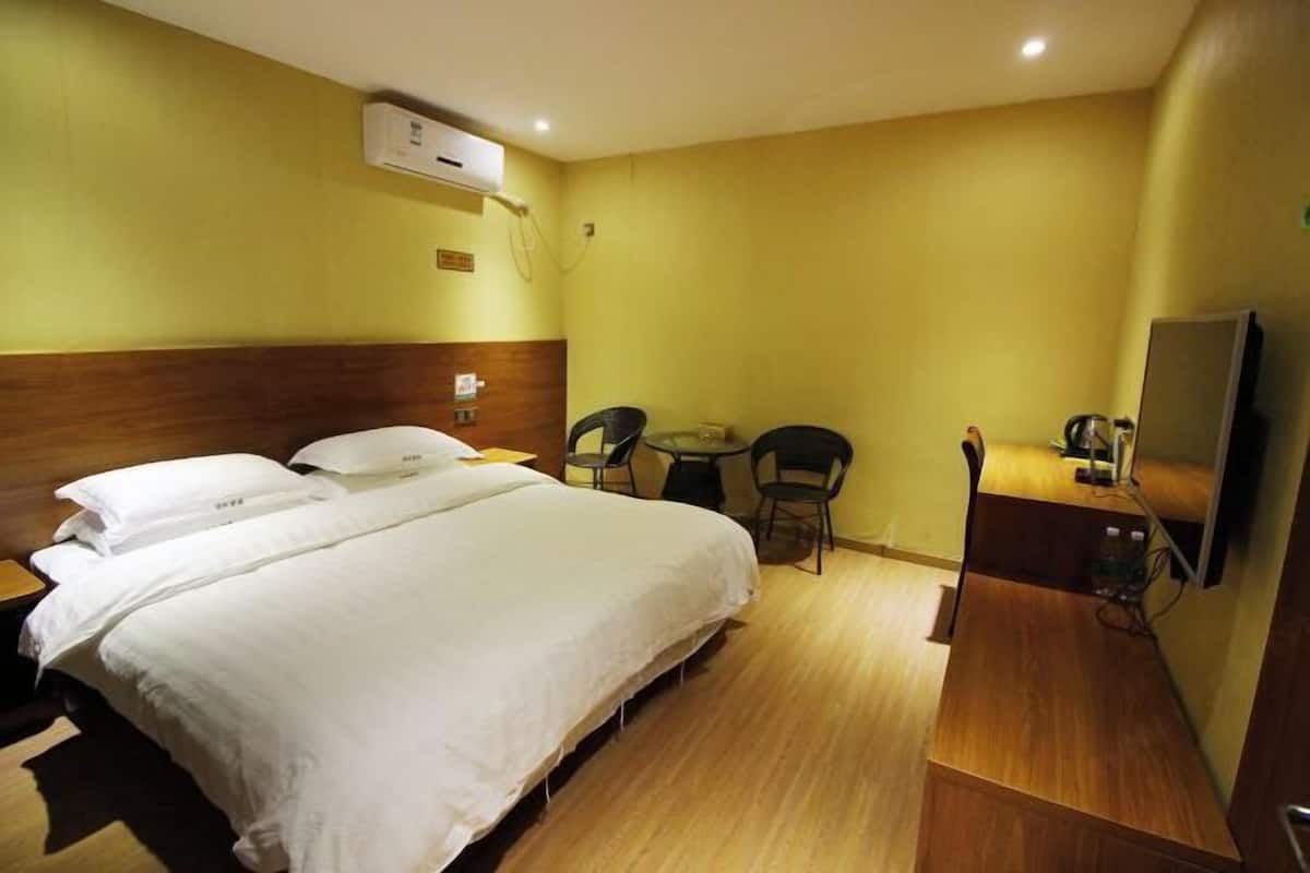 Hotellihuone, jossa on suuri sänky, työpöytä tuolilla, pieni pöytä ja televisio.
