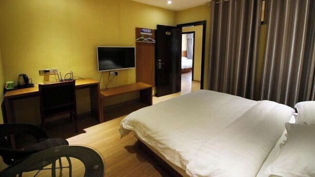 A hotel room with a bed, a desk with a chair, a television, and a wardrobe.