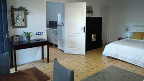 Kompakti hotellihuone, jossa on sänky, työpöytä tuolilla, pieni keittokomero ja vaatekaappi.