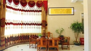 Une pièce avec une table ronde et des chaises, une grande fenêtre avec des rideaux et un panneau encadré accroché au mur.