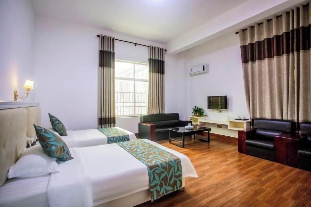 A hotel room with two beds, a sofa, a coffee table, and a TV.