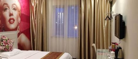 A hotel room with two beds, a desk with a chair, a television, and a large window with curtains.