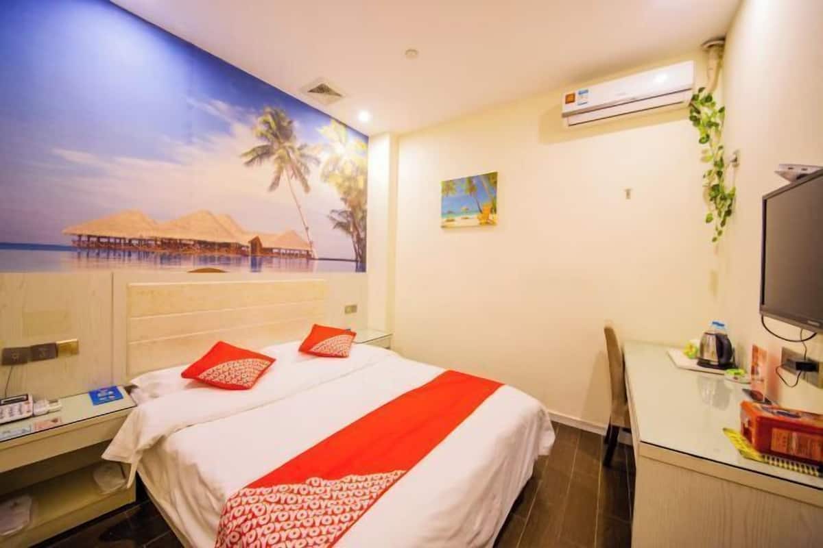 A hotel room with a bed, a desk, a television, and a wall with a tropical mural.