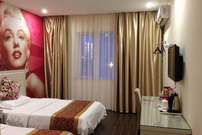 A hotel room with two beds, a desk, a chair, a television, and a large window with curtains.