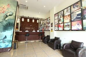 A reception area with a desk, chairs, and a wall with framed pictures. - Xinhuamian Fashion Hotel (Wenzhou)