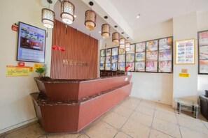 A reception area with a wooden reception desk, multiple framed pictures on the wall, and a tiled floor. - Xinhuamian Fashion Hotel (Wenzhou)