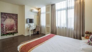 Habitación de hotel con una cama grande, un escritorio con silla, televisor y ventana con cortinas.