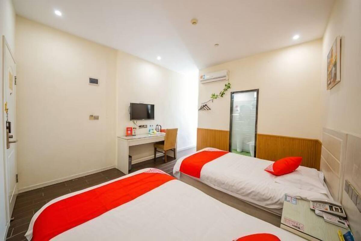 A hotel room with two beds, a desk with a computer, a TV, and a window.