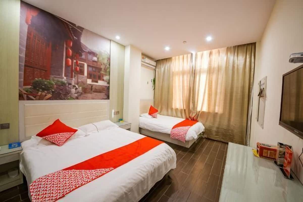 A hotel room with two beds, a TV, a desk, and a large window with curtains.
