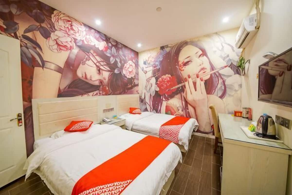 A hotel room with two beds, a desk, a chair, a mirror, and a large floral mural on the wall.