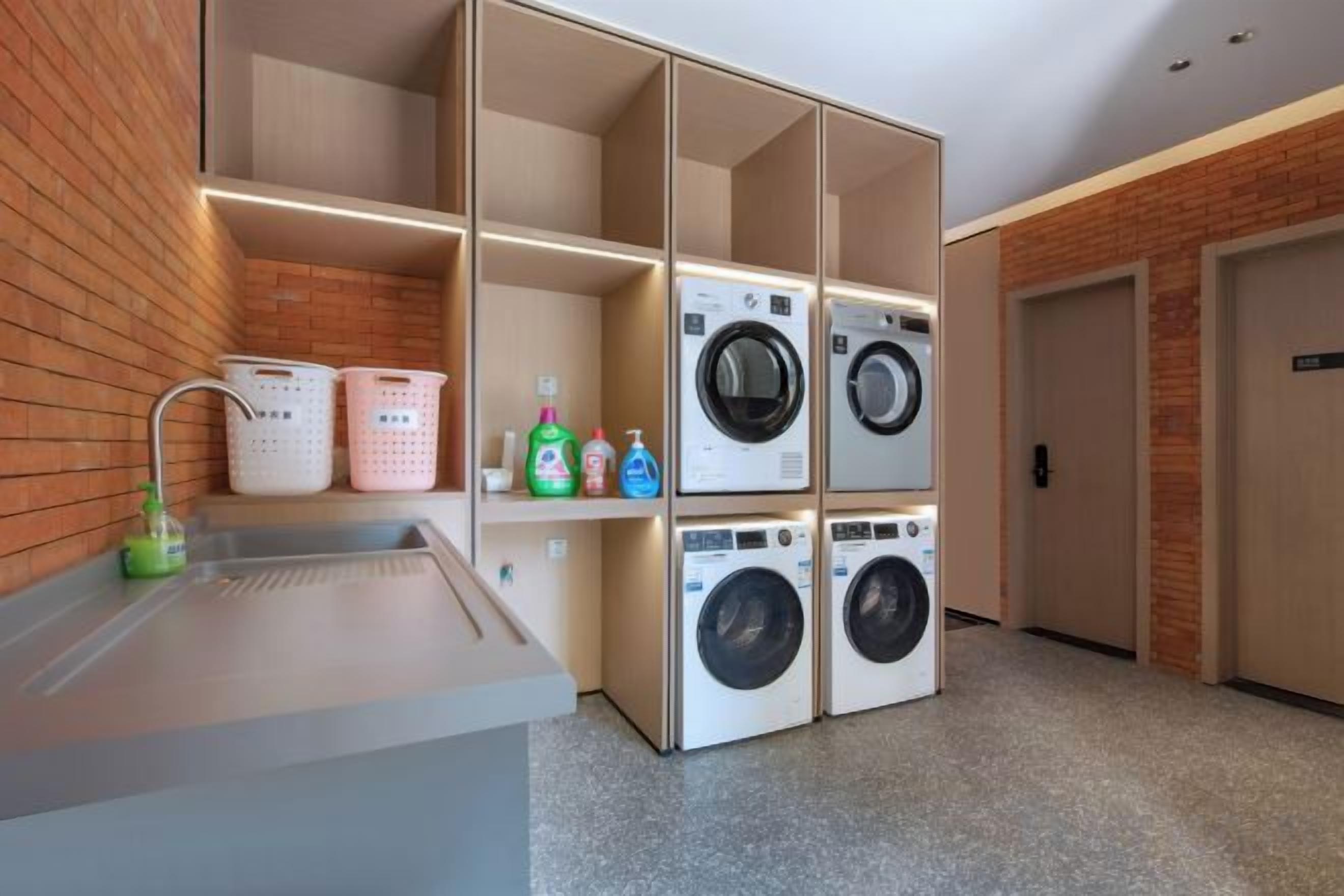 Un cuarto de lavandería con varias lavadoras, un lavamanos y estantes con útiles de limpieza.