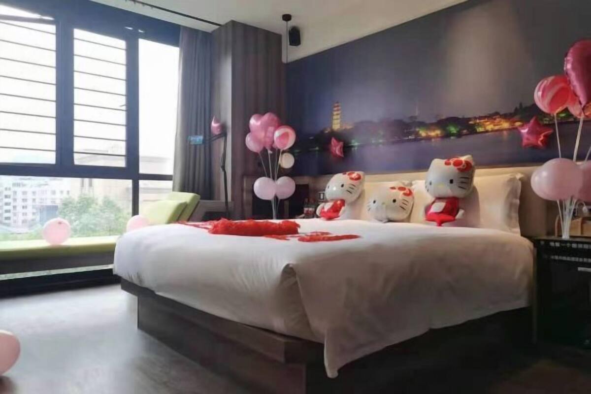 A hotel room with a large bed, a view of the cityscape through the window, and Hello Kitty decorations.