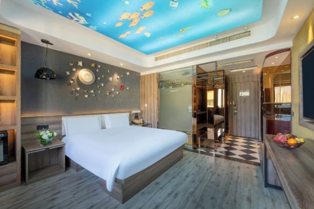 A modern hotel room with a large bed, a ceiling mural of fish, a glass shower enclosure, and a checkered floor.