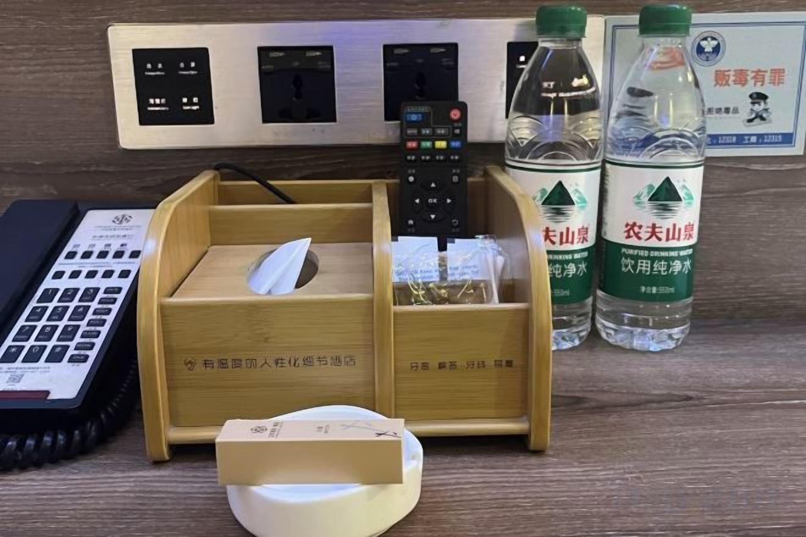 A desk with a keyboard, a remote control, a tissue box, and two water bottles.