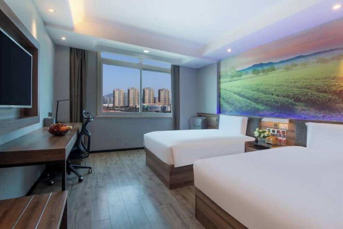 A hotel room with a large window, a desk with a chair, two beds, and a TV.