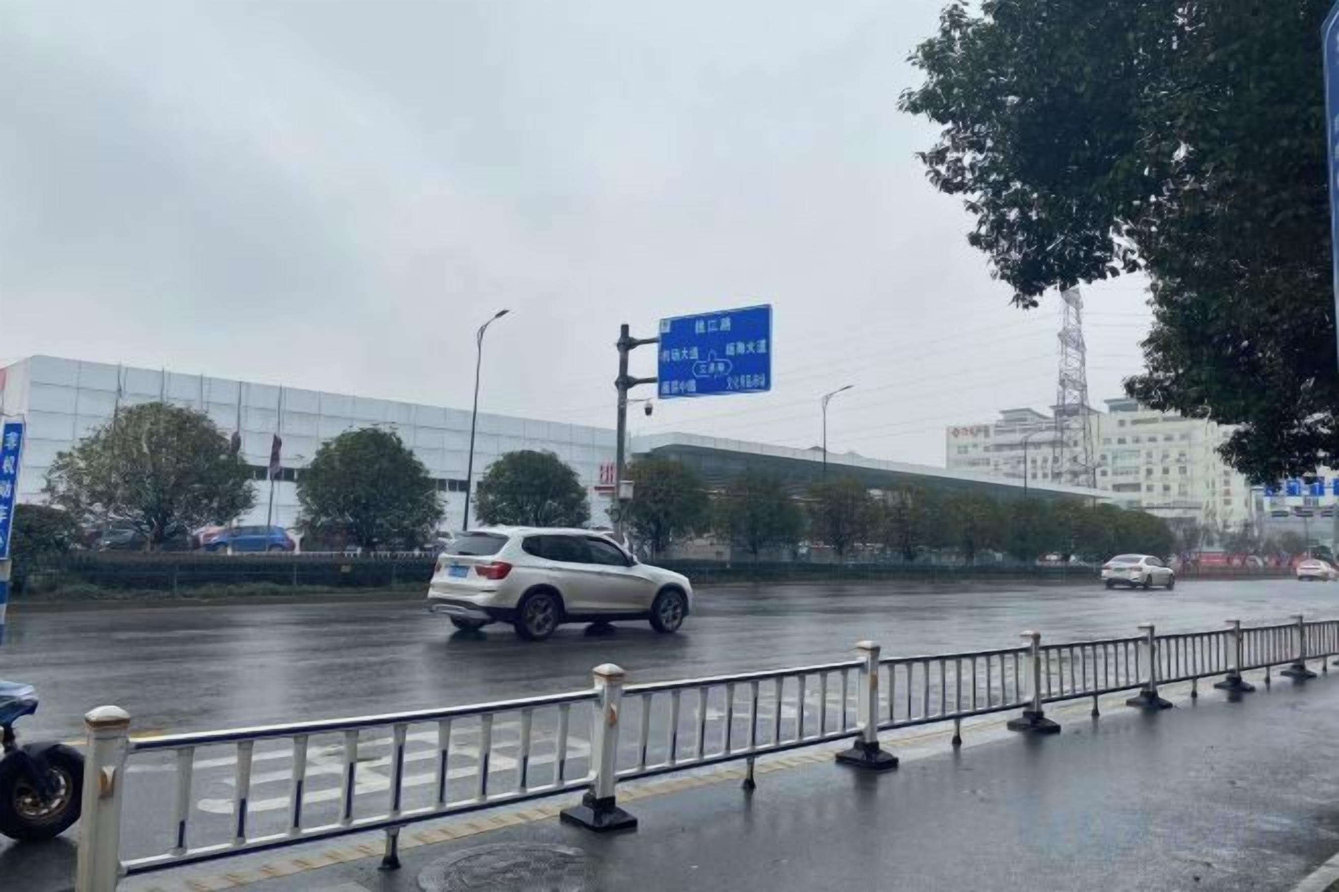 A wet road with a white car and a blue sign in the background.