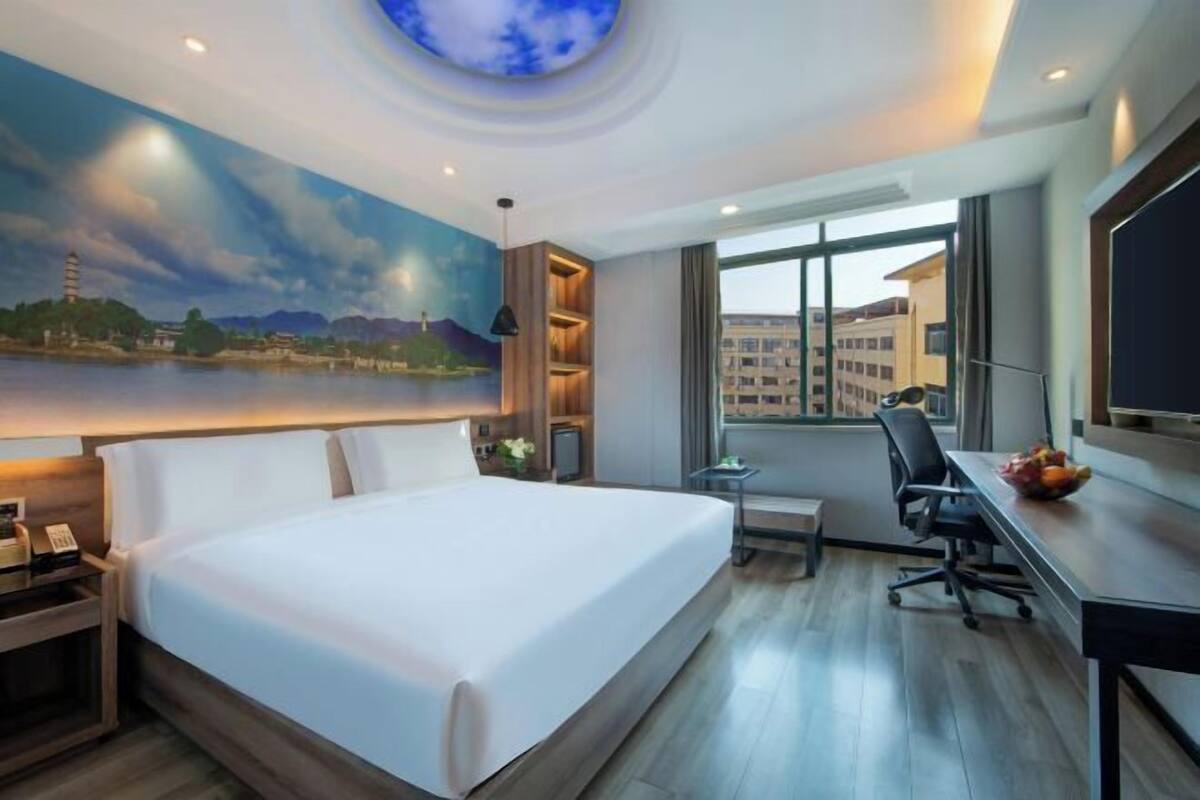 A hotel room with a bed, desk, chair, and a large window.