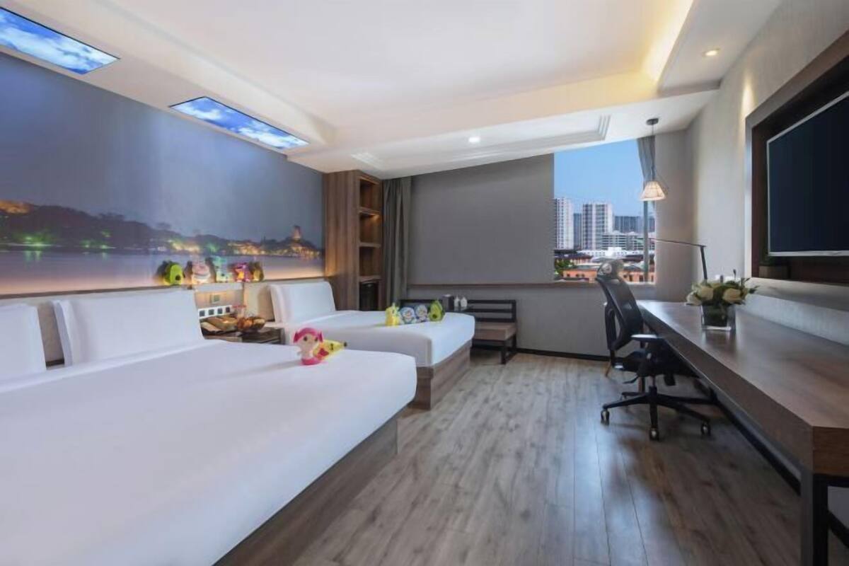 A modern hotel room with a large bed, a desk, and a view of the cityscape.