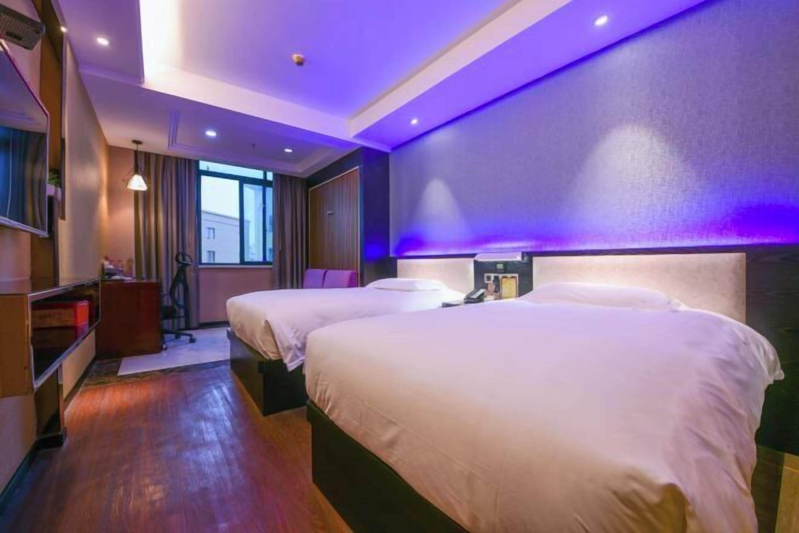 A hotel room with two beds, a desk, and a window.