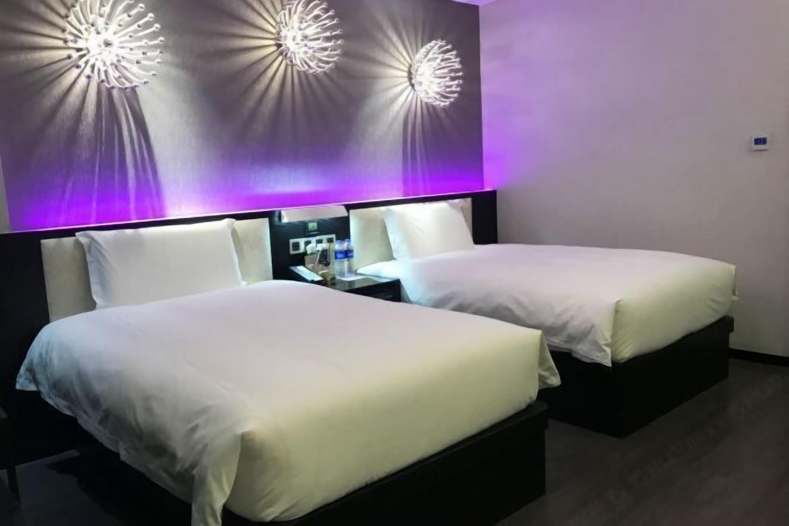 A hotel room with two beds, a nightstand, and decorative wall lights.